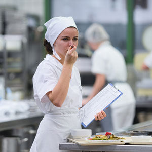 Diätassistentin probiert beim Einsatz in der Küche das frisch zubereitete Essen und kontrolliert die Qualität Diätassistentin probiert beim Einsatz in der Küche das frisch zubereitete Essen und kontrolliert die Qualität